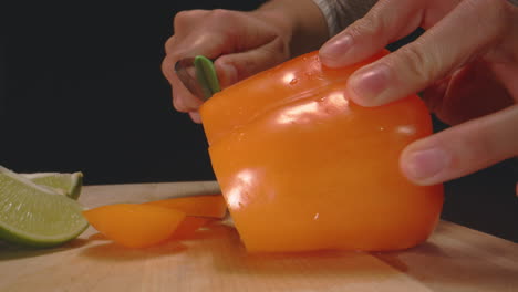 woman's hands cutting orange bell pepper with paring knife