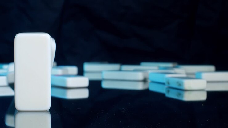 Front View of multi colored Dominoes Falling on a black reflective surface