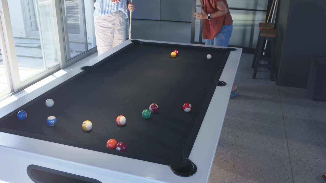 Diverse women in lounge watching center woman lining up, breaking on black felt pool table, playing
