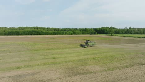 Aerial-establishing-view-of-combine-harvester-mowing-yellow-wheat,-dust-clouds-rise-behind-the-machine,-food-industry,-yellow-reap-grain-crops,-sunny-summer-day,-drone-shot-moving-forward,-tilt-down