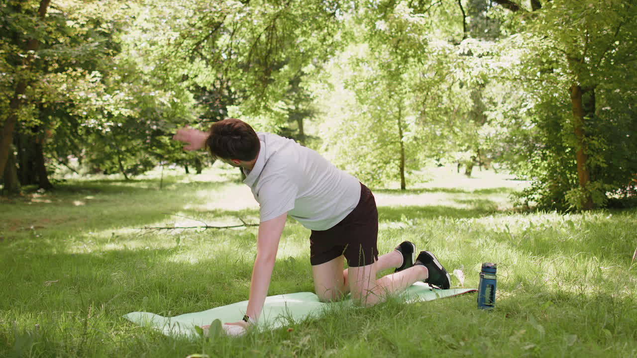 Fit flexible man doing workout yoga stretching on a sports mat in park raising arms exercising