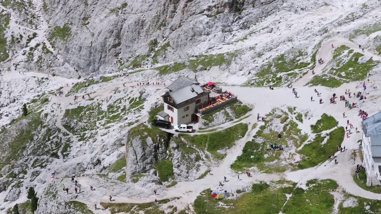 Top-down aerial of hikers and tourists at a mountain refuge nestled in a rocky valley in the Dolomites, Italy