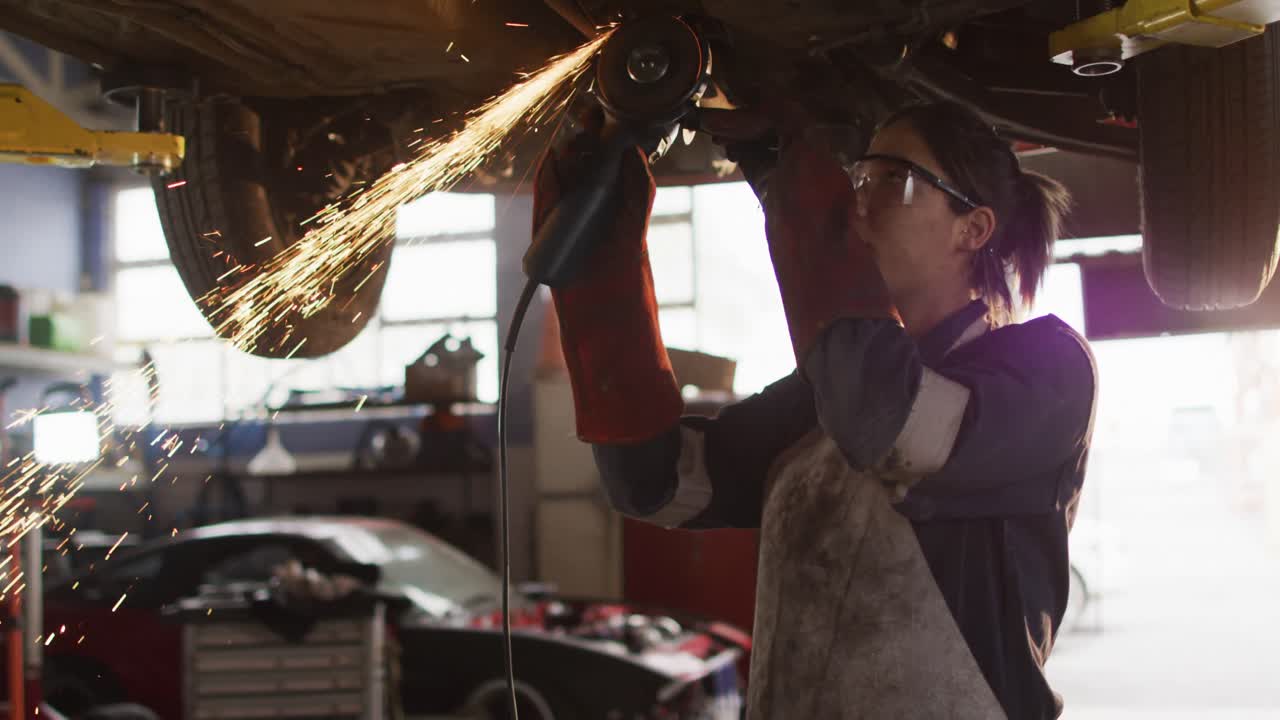 mecánica que usa un cortador de cuchillas eléctrico y trabaja debajo de un automóvil en una estación de servicio de automóviles