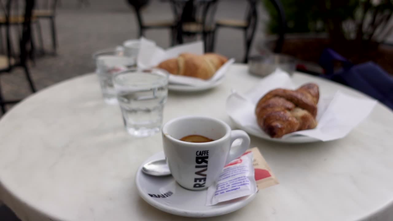 Woman serving an Espresso cup on a terrace's table with Italian croissant