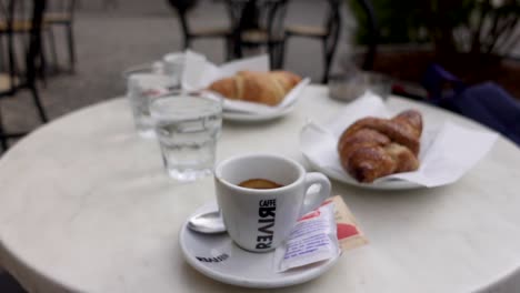 Mujer-Sirviendo-Una-Taza-De-Café-Expreso-En-La-Mesa-De-Una-Terraza-Con-Croissant-Italiano