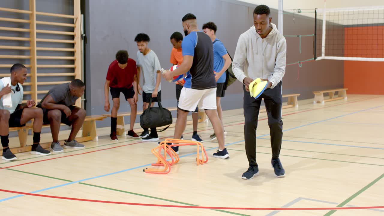 Männlicher Volleyballspieler folgt Teamkollegen, die Scheibenmarker auf dem Hallenboden platzieren, mit Platz für Text