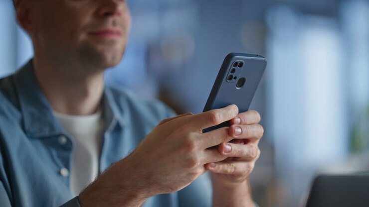 Lächelnder Mann tippt im Büro eine SMS auf seinem Handy. Mann genießt die Pause
