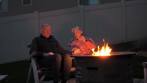 una pareja de mayores tomándose de la mano y hablando junto a un pozo de fuego en el patio trasero