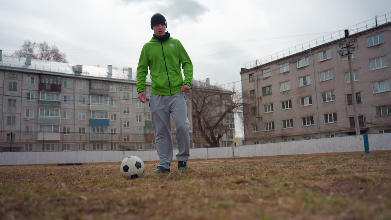 Un jugador regatea con seguridad, un hombre con una sudadera brillante controla el balón con confianza y una persona vestida con un atuendo de color verde vivo maneja hábilmente el balón mientras se mueve hacia la cámara con una actitud serena.