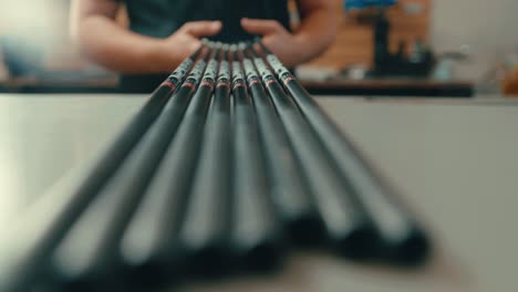 manos masculinas agarrar un conjunto de ejes de club de golf fuera de la encimera en el taller en cámara lenta