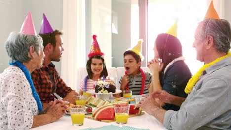 animation of white confetti falling over happy multi generation family having birthday party