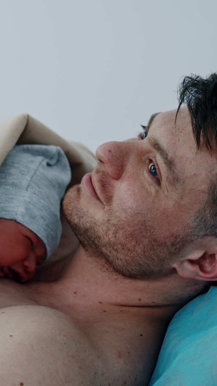 Caucasian father holding his newborn baby on the bare chest. Little child cries bitterly. Infant born through C-section. Vertical video