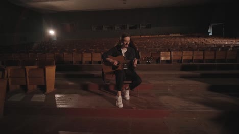 a handsome guy plays an acoustic guitar in an abandoned cinema. the musician sings a song and accompanies on the guitar