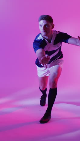 video vertical de un jugador de rugby caucásico atrapando una pelota de rugby sobre la iluminación rosa