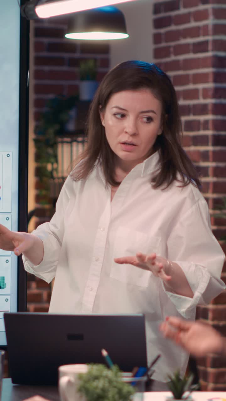 Vertical video: Businesswoman giving presentation in business meeting, holding laptop