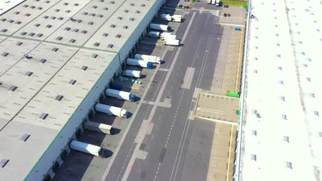 Aerial-view-of-a-semi-trucks-with-cargo-trailers-standing-on-warehouses-ramps-for-loading-unloading-goods-on-the-big-logistics-park-with-loading-hub