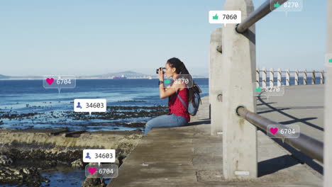 social media engagement animation over woman photographing ocean from pier