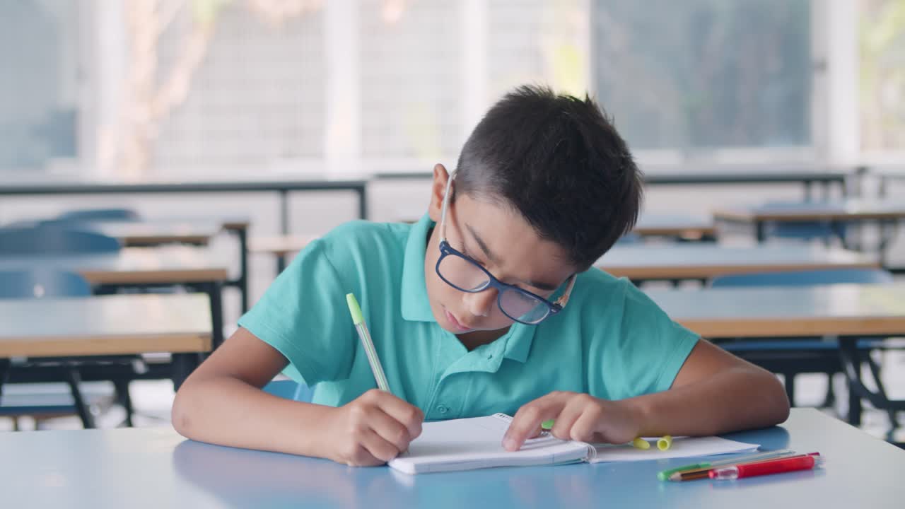 niño alumno latino enfocado con gafas escribiendo en papel