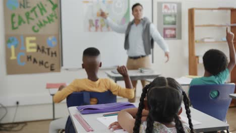 Diverse-male-teacher-and-children-raising-hands-at-desks-in-elementary-school-class,-slow-motion