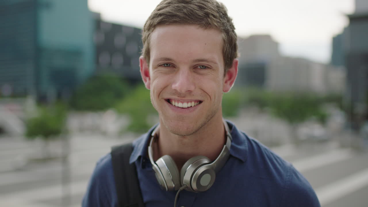 close up portrait of happy young caucasian man student looking at camera laughing cheerful on college campus in city background