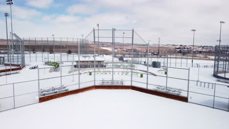 Tilt-down-of-baseball-and-softball-field-backstop-during-the-winter-with-snow,-aerial