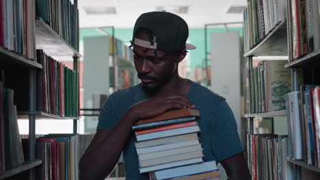 Joven con gorra transporta una pila de libros por el pasillo de una biblioteca, se detiene y examina las estanterías en busca de un lugar donde colocar los volúmenes, ambiente de estudiante reflexivo, entorno de estudio tranquilo, luz de día suave