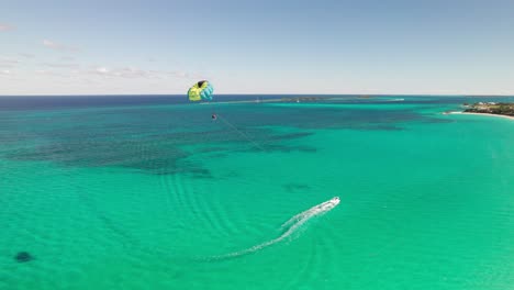 Parasailing-in-the-Caribbean,-gorgeous-turquoise-water-with-sand-and-reefs