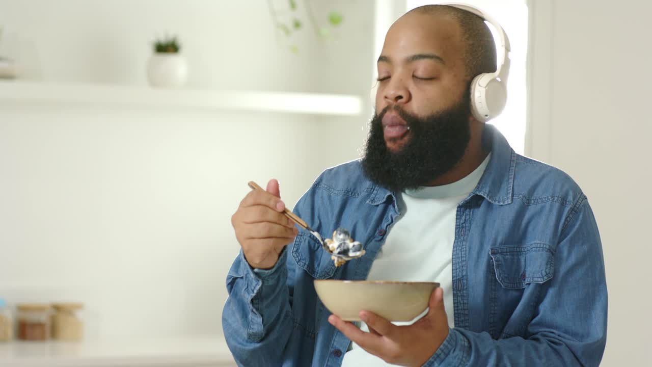 Hunger driving African American man in shirt eating yogurt from bowl with spoon donning headphones