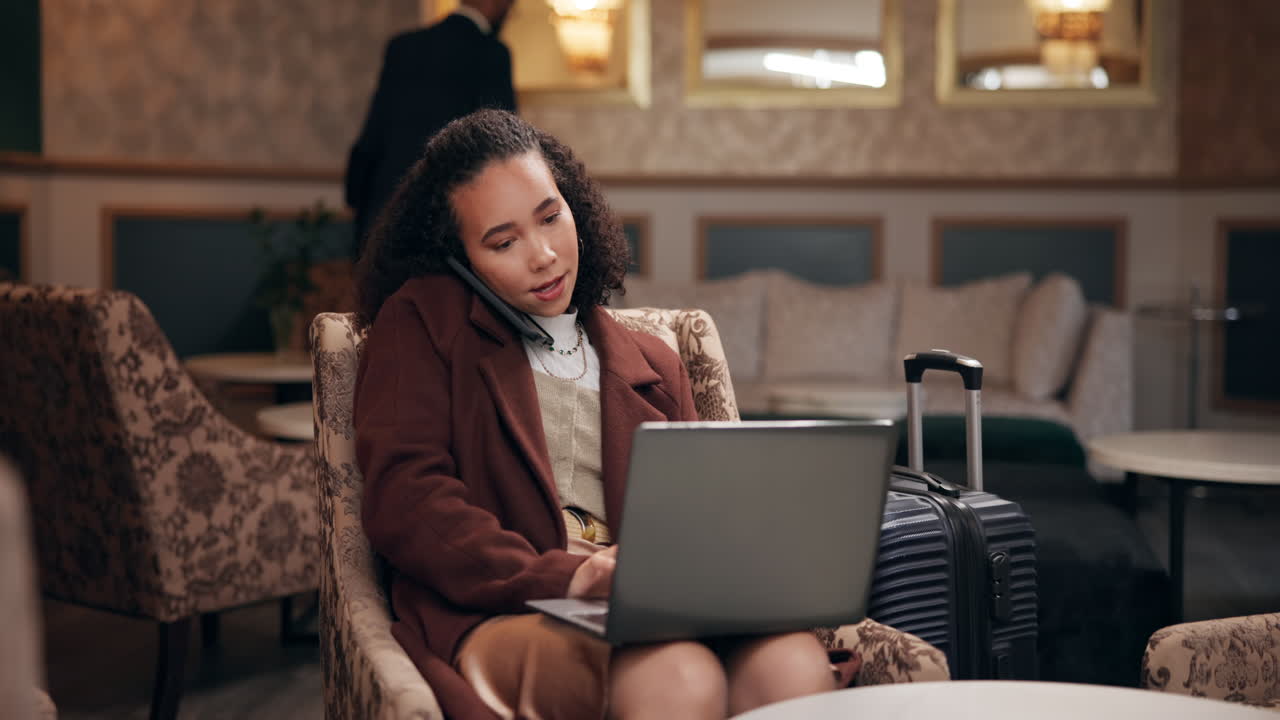 Woman working on laptop and talking on phone in hotel lobby
