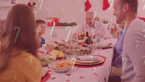 Animation-of-candy-canes-falling-over-smiling-caucasian-family-having-dinner