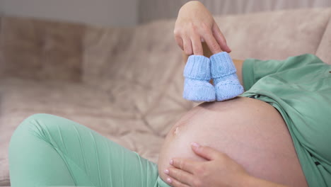 pregnant woman holding knitted socks on a bare belly. beautiful warm blue shoes for a future baby in woman's hands. expecting a child.