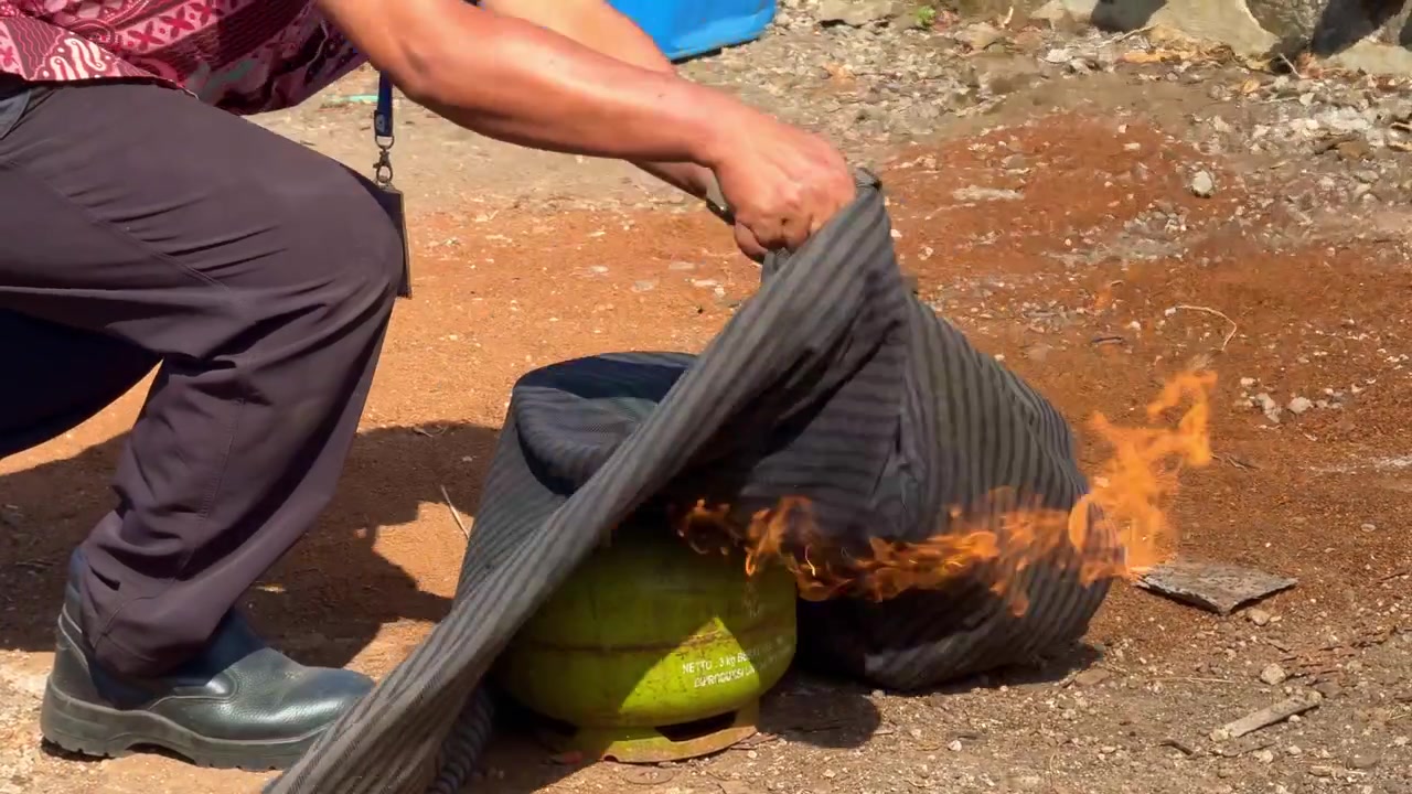 Pessoa cobrindo fogo em cilindro de gás com manta molhada para treinamento de segurança. Vídeo conceitual de segurança contra incêndio, simulado de emergência e perigo de GLP.