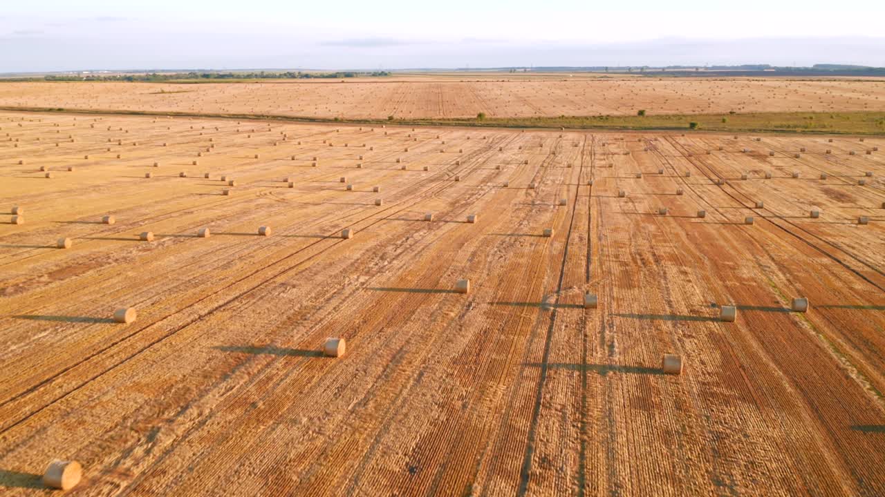 Drone flying above picturesque farmland with golden haystacks on a sunny day.