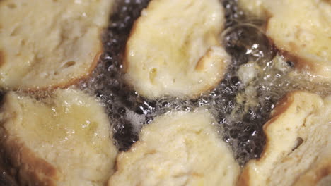 yellow creamy egg soaked round pieces of bread frying to make rabanadas - high angle extreme close up