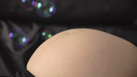 Bubbles float around and pop on a close-up shot of a pregnant belly that&#039;s ready to pop