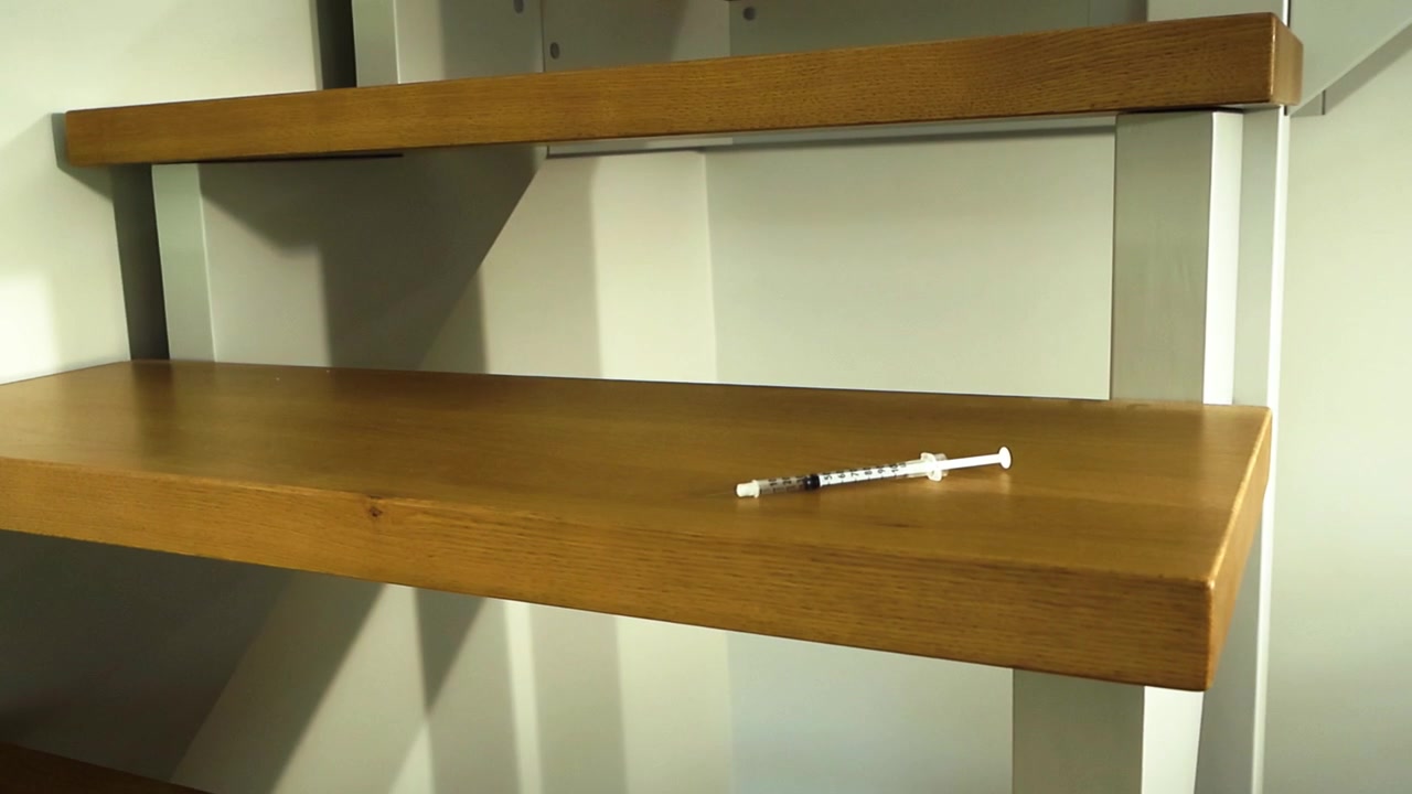 Jeringa abandonada con heroína u otro narcótico ilegal sobre los escalones de madera de una escalera de casa moderna, simbolizando la trágica realidad de la adicción a las drogas, el abuso y la dependencia.