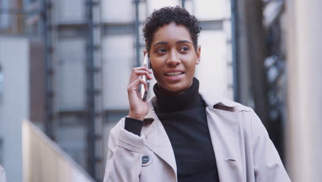 fashionable young black woman standing in a business area of the city talking on her smartphone, close up, focus on foreground