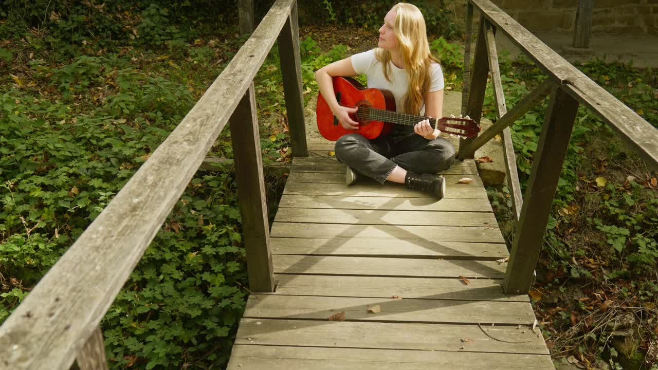 una joven rubia hermosa toca la guitarra acústica y el puente de madera