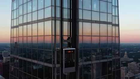a captivating view of a high-rise elevator ascending through the glass facade of a modern skyscraper at dusk with striking reflections in the setting sun