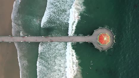 Gente-Surfeando-Y-Algunos-Yendo-Al-Acuario-De-Casa-Redonda-En-El-Muelle-De-La-Playa-De-Manhattan-En-California