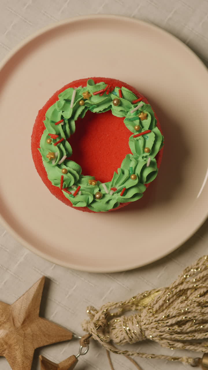 Close-up of a mini red cake decorated like a Christmas wreath as a fork cuts a slice, surrounded by festive and warm details