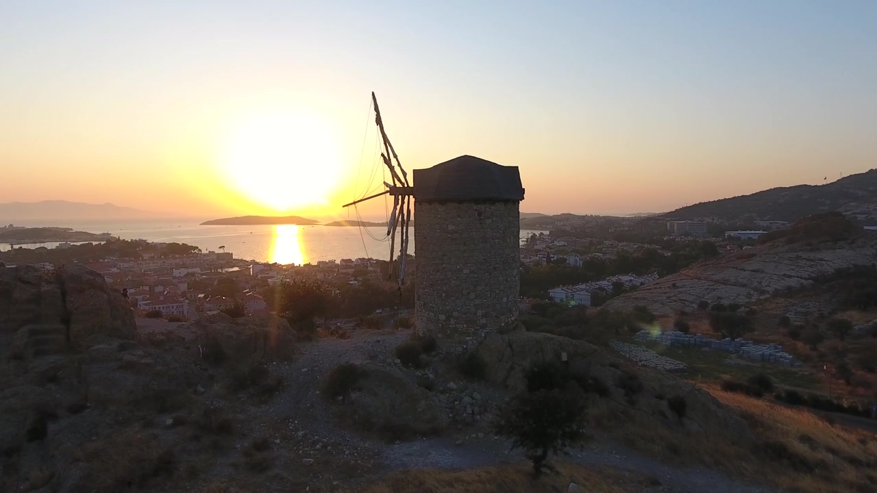 Antigo Moinho de Vento de Pedra com Vista para uma Cidade Costeira ao Pôr do Sol