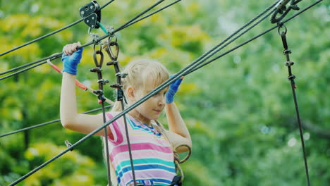 entertainment in summer camp - a child learns to use insurance cables climbs high in the branches of