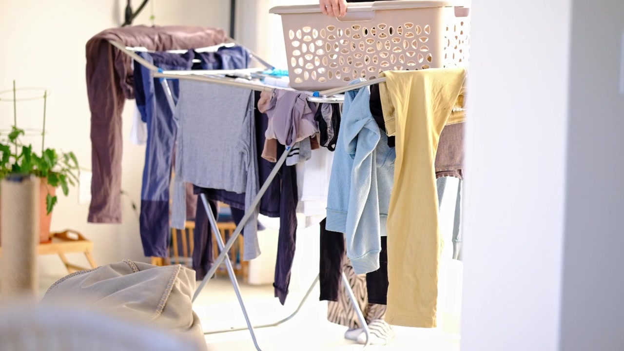 Woman removing laundry from a clothes horse into a basket inside a home