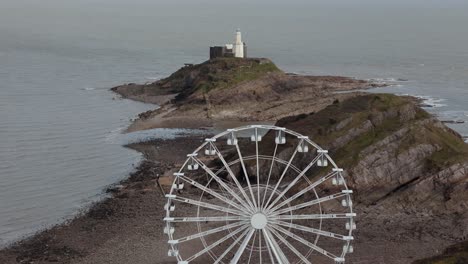 the big wheel rotating with a mumbles lighthouse at background in mumbles pier swansea of england. aerial view.