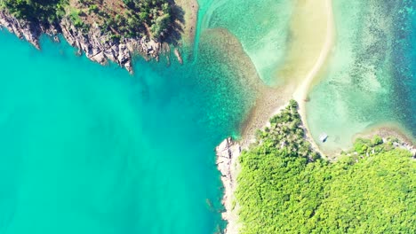 Green-vegetation-of-tropical-island-with-rocky-coastline-washed-by-calm-turquoise-lagoon-full-of-coral-reefs-in-Thailand