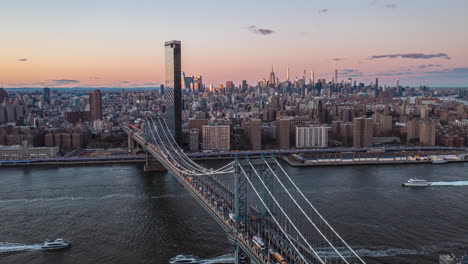 Forwards-fly-over-Manhattan-bridge.-Heavy-traffic-on-roads-and-on-water.-Skyline-with-downtown-skyscrapers-against-pink-twilight-sky.--Manhattan,-New-York-City,-USA