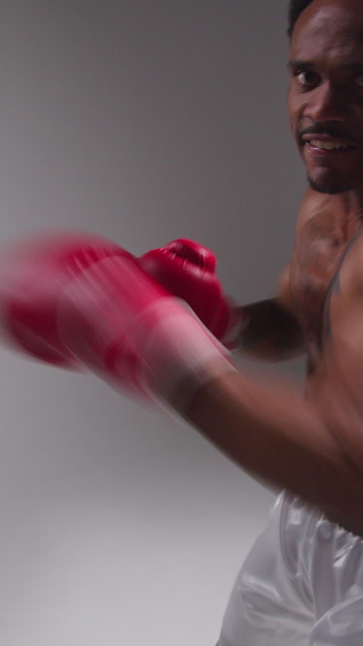 Video verticale, ripresa in tempo reale in studio in POV di un pugile maschio tatuato che indossa guantoni da boxe in un incontro di boxe, mentre sferra pugni verso la telecamera