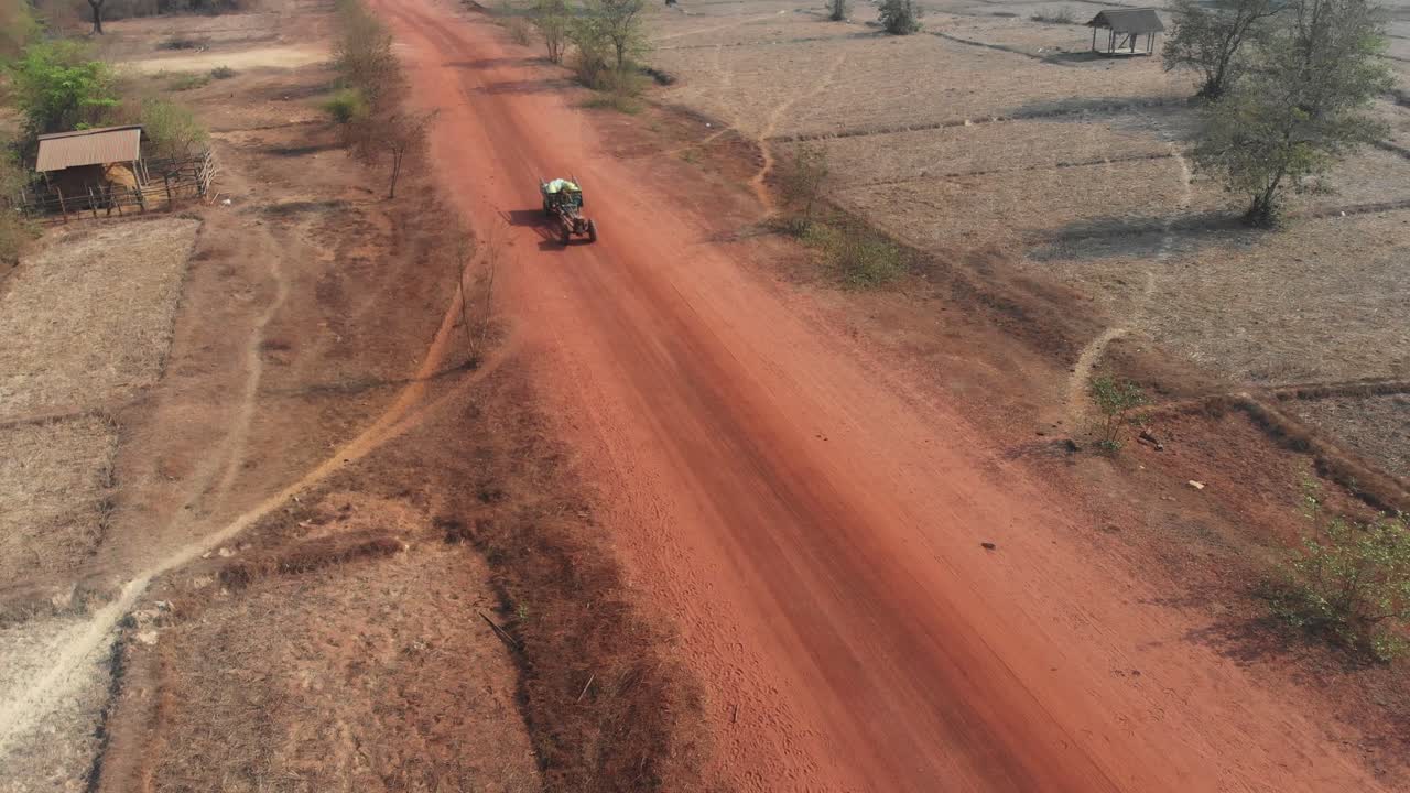 Trattore con rimorchio che percorre una strada sterrata in Laos, ripresa aerea
