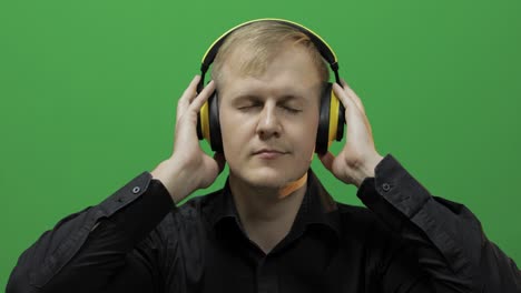 Guy-listens-to-music-in-wireless-yellow-headphones-and-dances.-Green-screen